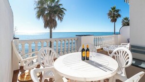 Una mesa redonda con sillas en un balcón con vistas al mar, con dos botellas de vino y una copa.