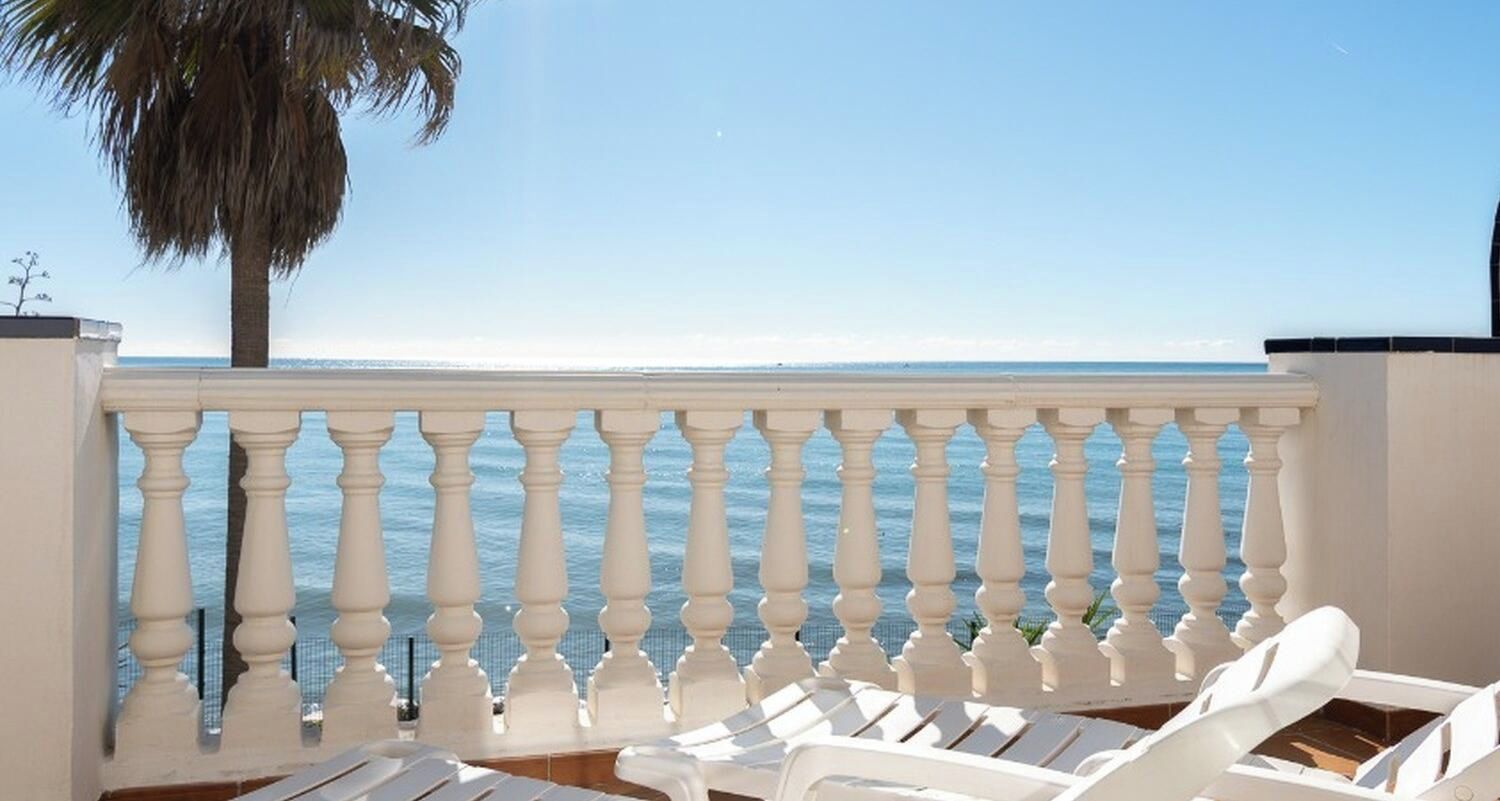Ein Balkon mit weißer Brüstung mit Blick auf einen Strand.