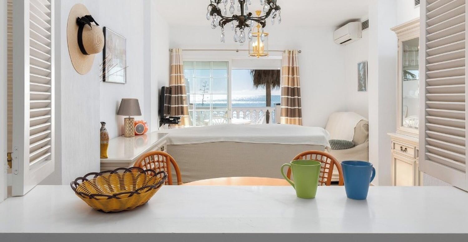Ein Hotelzimmer mit Bett, Esstisch mit Stühlen, einer Chandelüster und Blick aufs Meer.