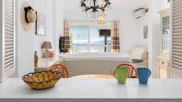 Ein Hotelzimmer mit Bett, Esstisch mit Stühlen, einer Chandelüster und Blick aufs Meer.