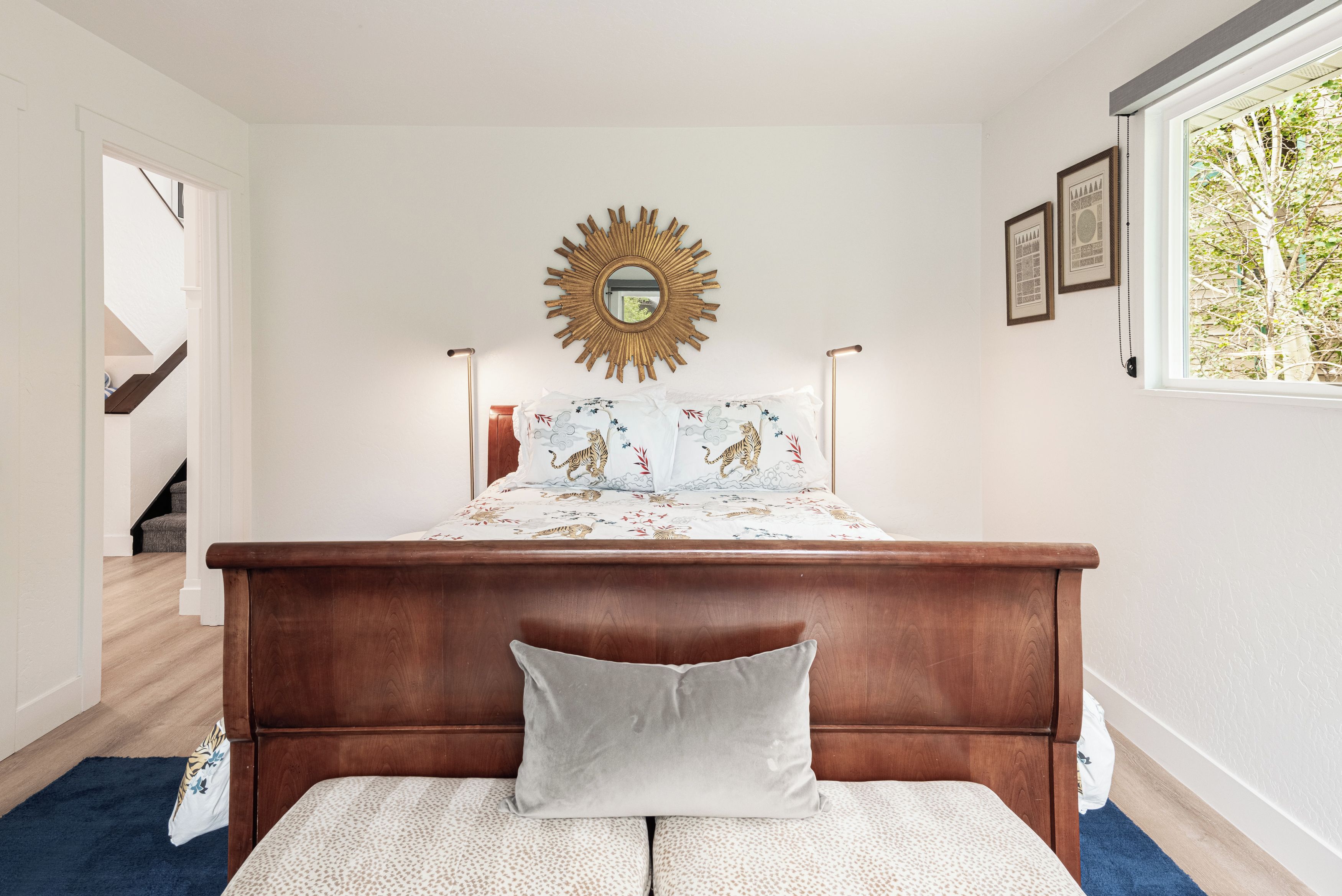 Une chambre à coucher avec une tête de lit en bois, un miroir en forme de soleil et un lit doté d’une literie à motifs de tigres.