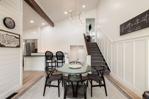 A modern kitchen with a dining area, featuring a round glass table with chairs, a chandelier, and a staircase leading to an upper level. - Spacious 4BR townhome for 10 in Park City's Prospector Square. (Park City)