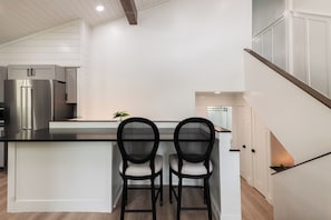 A modern kitchen with a central island, two bar stools, a stainless steel refrigerator, and a staircase leading to an upper level. - Spacious 4BR townhome for 10 in Park City's Prospector Square. (Park City)