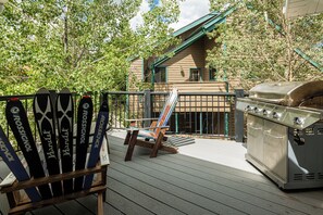 Eine Terrasse mit Grill, einem Stuhl und abgestellten Skiern an einem Zaun.