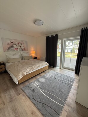 Ein Schlafzimmer mit einem Bett, einem Nachttisch, einer Lampe, einem Gemälde und Blick ins Freie.