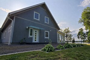 A two-story house with a gabled roof, a front porch, and a small garden area with plants. - Schweden-Auszeit: Lake Lodge mit Wintergarten, Sauna, Kamin & Boot direkt am See (Alsterbro ( Schweden))