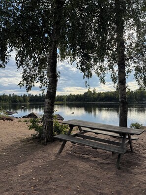 Ein Picknickplatz am Seeufer mit einer hölzernen Bank, Bäumen und einem ruhigen See.