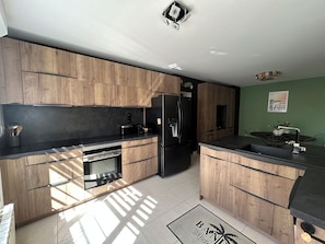 Eine moderne Küche mit Holzschränken, einem schwarzen Kühlschrank und einem eingebauten Backofen.