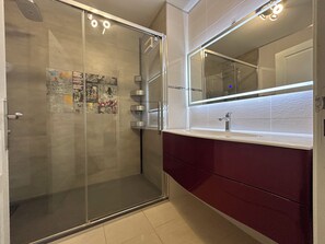 Ett modernt badrum med en duschavdelning med glasväggar, en tvättställsmöbel med spegel och en kakelbeklädd vägg bakom tvättstället.