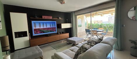 A modern living room with a flat-screen TV, a sofa, a coffee table, and a sliding glass door leading to an outdoor patio.