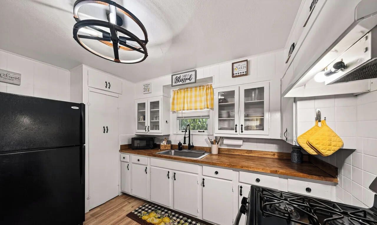 A kitchen with white cabinets, a black refrigerator, a wooden countertop, a gas stove, and a yellow towel hanging on the wall.
