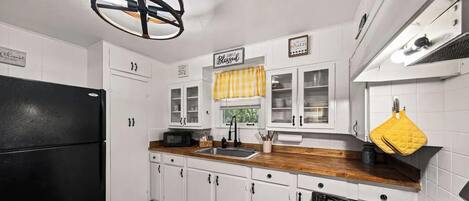 A kitchen with white cabinets, a black refrigerator, a wooden countertop, a gas stove, and a yellow towel hanging on the wall.
