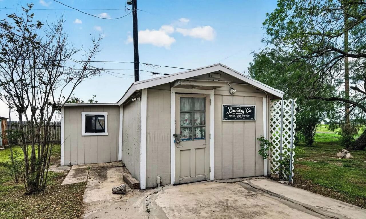 A small, single-story laundry facility with a door and window, surrounded by a fence and trees.