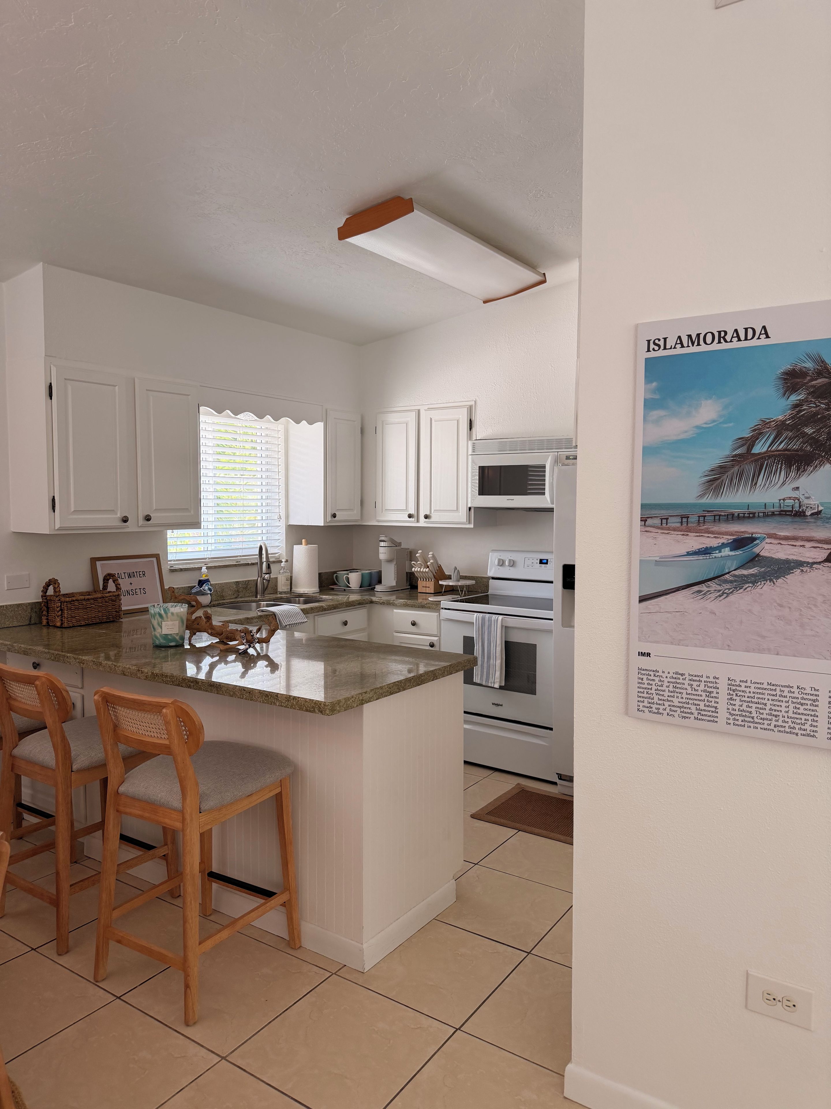 A kitchen with white cabinets, a central island with bar stools, a microwave, and an oven.