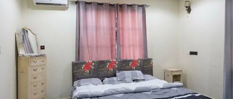 Un dormitorio con cama, cómoda, aire acondicionado y mesita de noche.