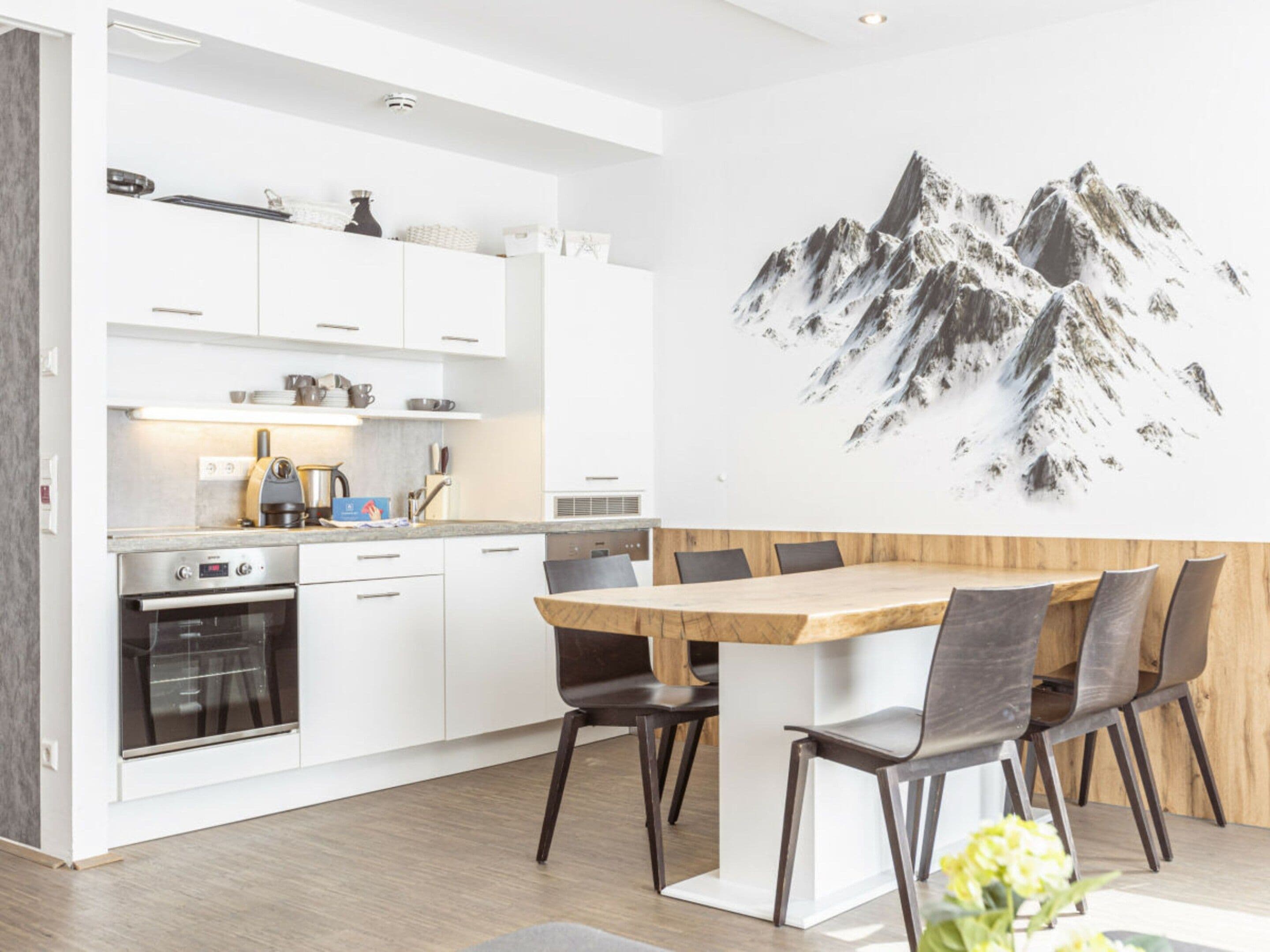 A modern kitchen with white cabinets, a built-in oven, and a dining area with a wooden table and chairs.