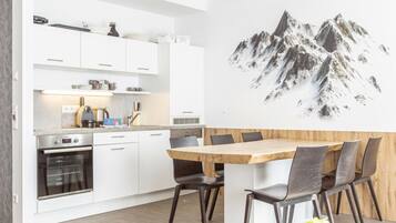 A modern kitchen with white cabinets, a built-in oven, and a dining area with a wooden table and chairs.