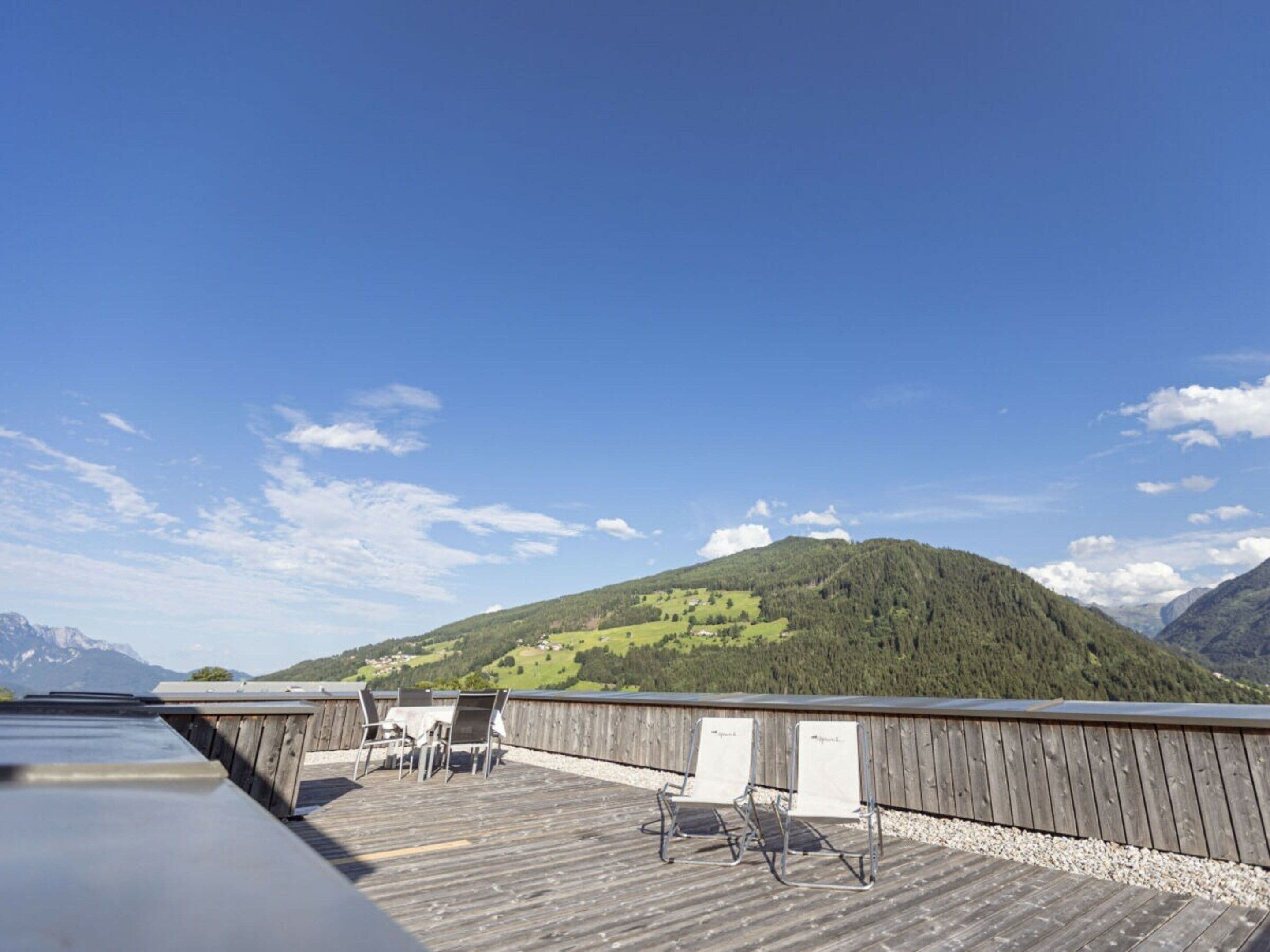 En træterrasse med udendørs møbler og udsigt til et bjerg.
