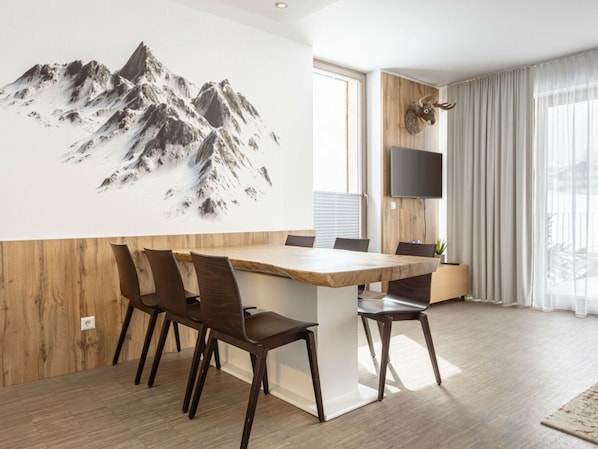 A modern dining area with a wooden table and chairs, a large wall-mounted TV, and a mountain artwork. - Apartment With 1 Bedroom (Schladming)