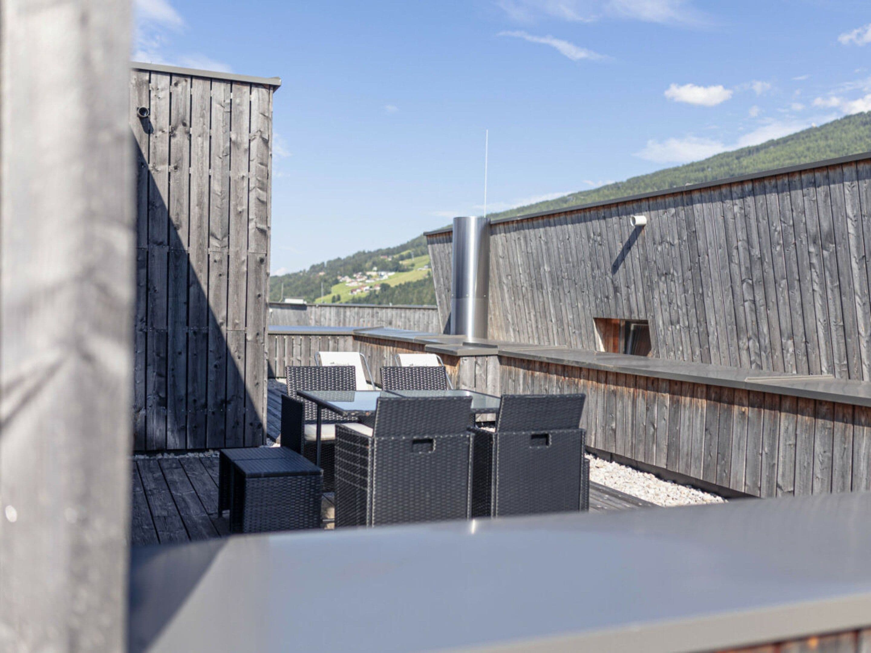 A rooftop terrace with outdoor seating and a view of a hilly landscape.