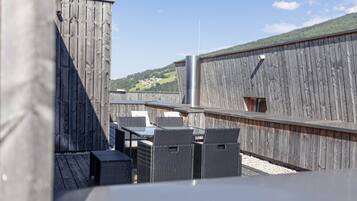 A rooftop terrace with outdoor seating and a view of a hilly landscape.