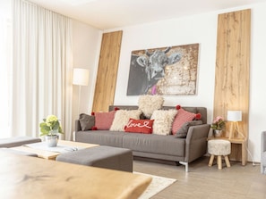 A modern living room with a grey sofa, red and white pillows, a wooden coffee table, and a painting of a cow on the wall. - Apartment With 1 Bedroom (Schladming)