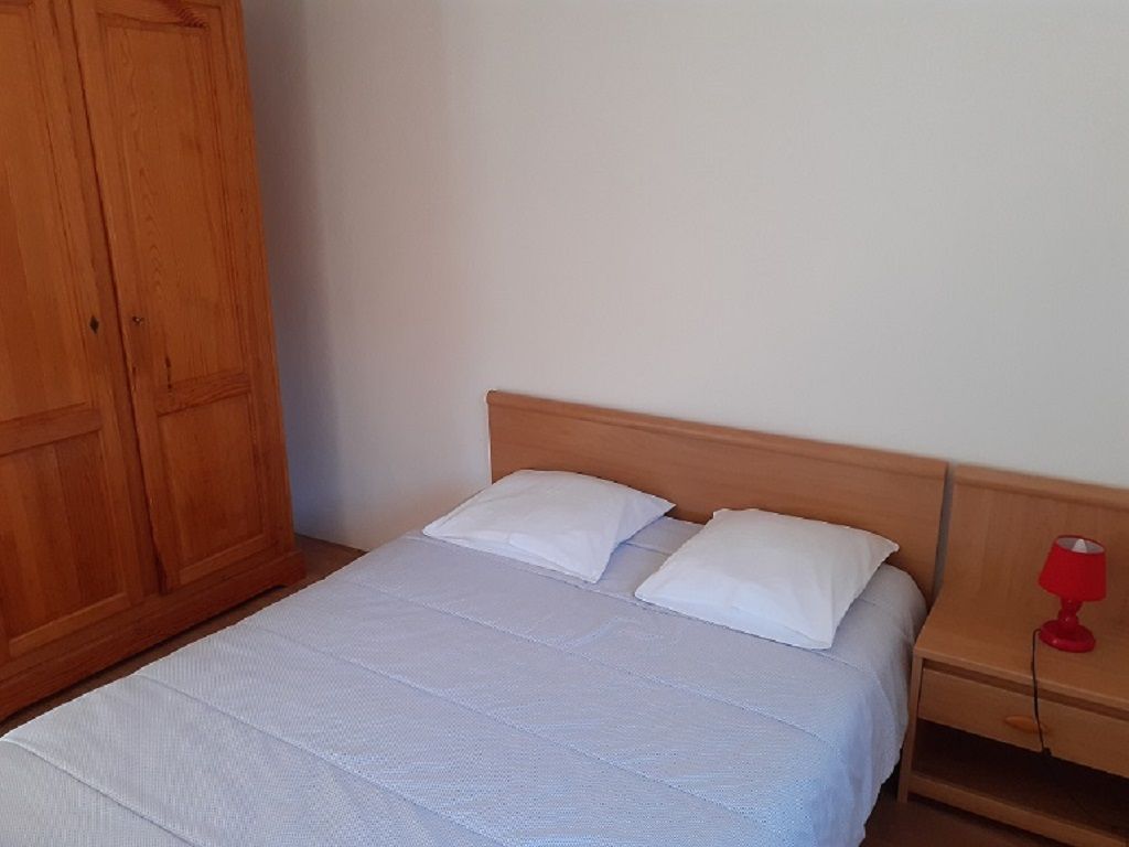 A single bed with a wooden headboard, a nightstand with a red lamp, and a wooden wardrobe.