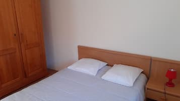 A single bed with a wooden headboard, a nightstand with a red lamp, and a wooden wardrobe.