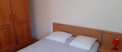 Una cama individual con cabecera de madera, una mesita de noche con una lámpara roja y un armario de madera.