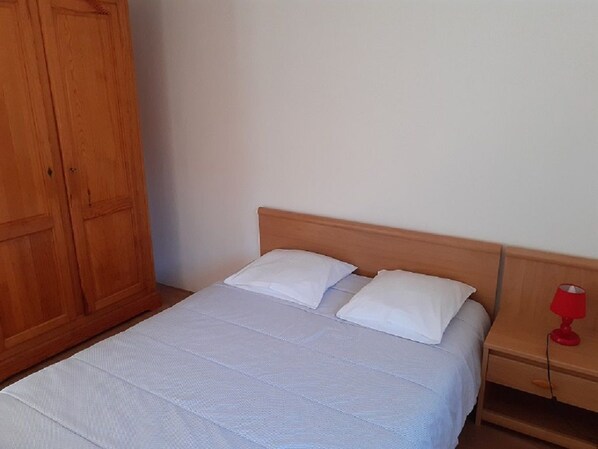 A single bed with a wooden headboard, a nightstand with a red lamp, and a wooden wardrobe.