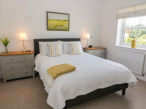 A bedroom with a bed, two bedside tables, a nightstand, a window with a view, and a painting on the wall. - The Croft (Ashbourne)