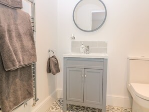A bathroom with a toilet, a sink with a mirror above it, and a towel rack with towels. - The Croft (Ashbourne)