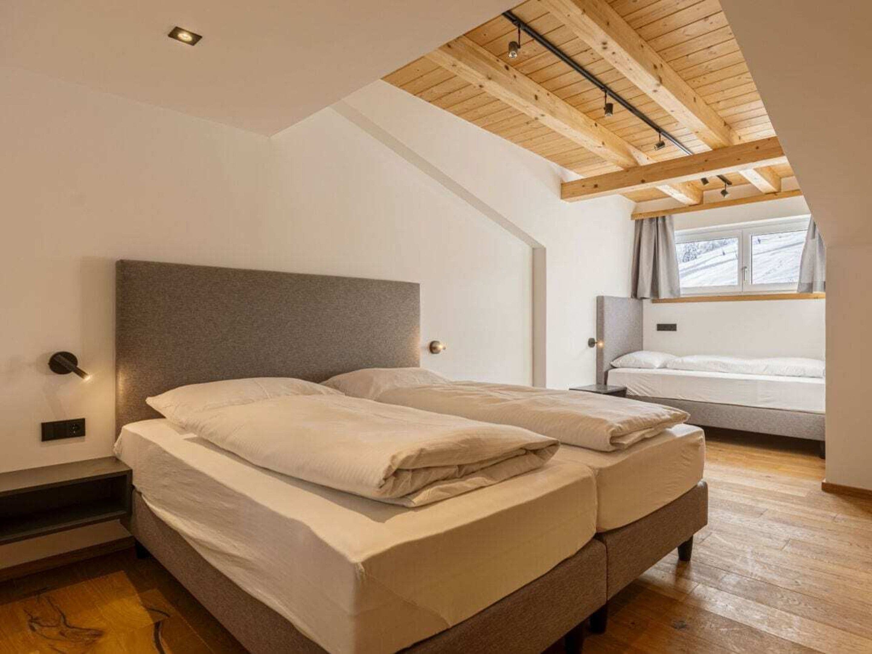 A bedroom with a large bed, a window with curtains, and a wooden ceiling.