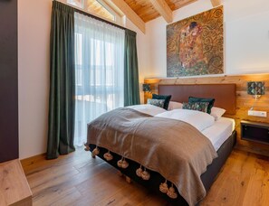 Ein Schlafzimmer mit einem großen Bett, einem Holzkopfstück, einem Gemälde über dem Bett und einem Fenster mit Vorhängen.