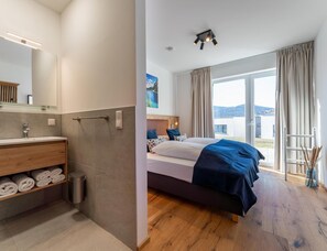 A hotel room with a bathroom, a bed with a view, and a wooden floor. - Chalet Right Next to the ski Area (Sankt Lambrecht)