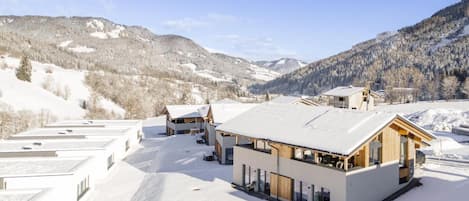A modern building with a flat roof, large windows, and a snow-covered landscape in the background.