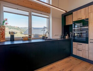 Eine moderne Küche mit einem großen Fenster, dunklen Schränken und einem eingebauten Backofen.