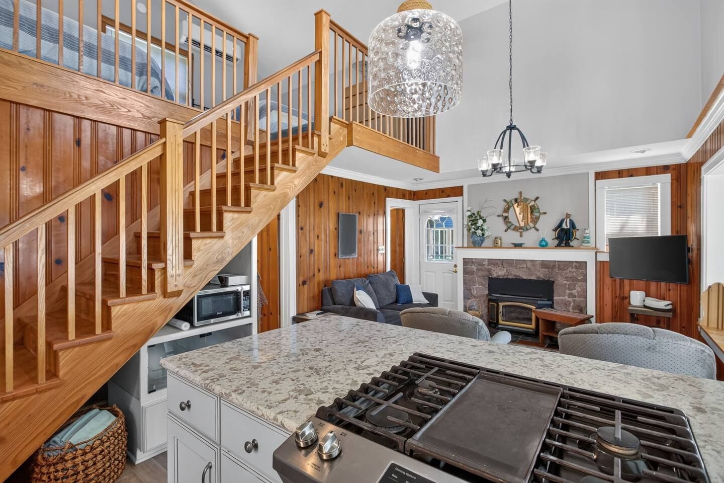 A modern kitchen with a built-in stove, wooden staircase, and a dining area with a large island.
