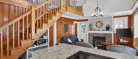 A modern kitchen with a built-in stove, wooden staircase, and a dining area with a large island.