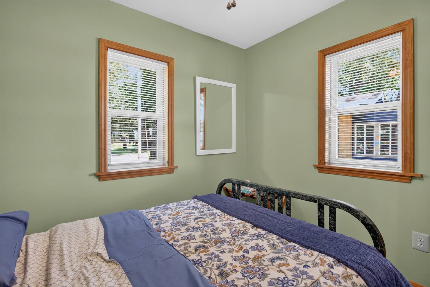 A bedroom with a bed, two windows with blinds, a mirror, and a ceiling light fixture.