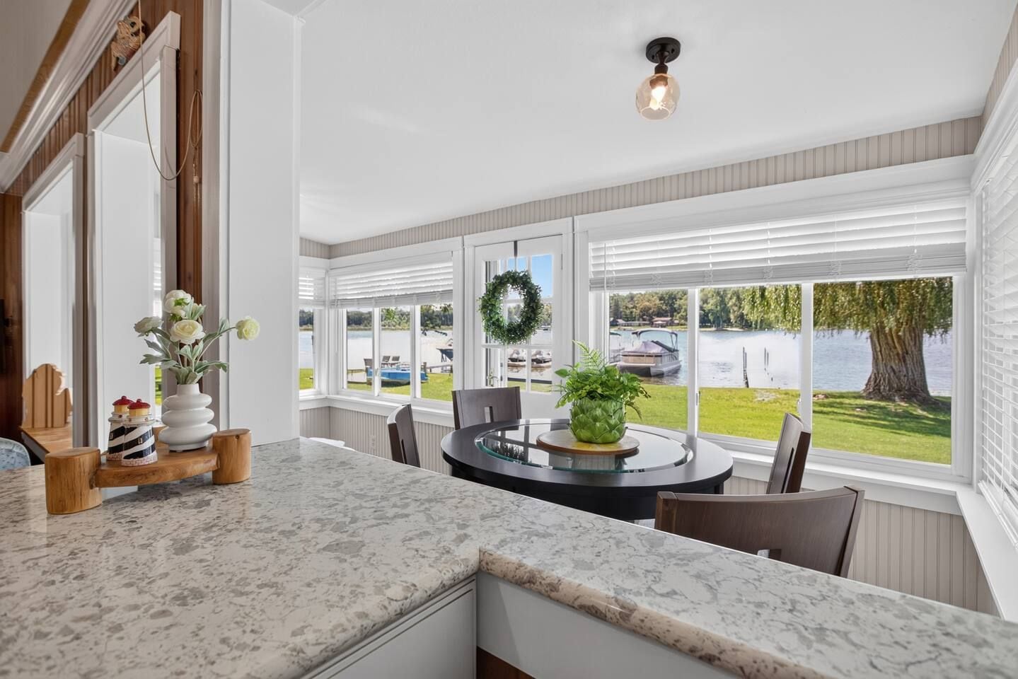 A kitchen with a marble countertop, a dining table with chairs, and large windows with a view of a lake and boats.