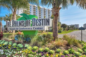 A sign for The Palms of Destiny Resort & Conference Center with a large palm tree and colorful flowers in the foreground. - 🌴Beach Nearby + Lagoon Pool | Gulf View | Palms 11203☀️ (Destin)