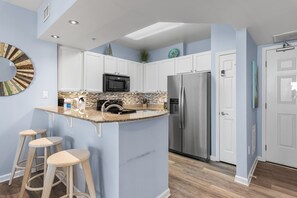 A kitchen with a central island, white cabinets, a stainless steel refrigerator, and a microwave. There are two stools at the island. - 🌴Beach Nearby + Lagoon Pool | Gulf View | Palms 11203☀️ (Destin)
