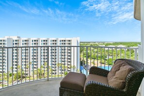 A balcony with a wicker sofa and a view of a high-rise building and a golf course. - 🌴Beach Nearby + Lagoon Pool | Gulf View | Palms 11203☀️ (Destin)