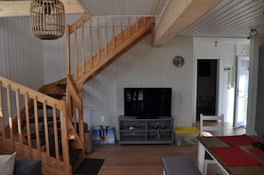 A wooden staircase leading to a loft area, a flat-screen TV on a grey stand, and a white door leading to another room. - Ferienhaus Frida (Wandlitz)
