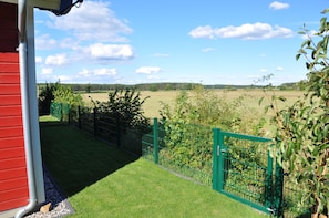 A view from a balcony with a red building, a green fence, and a field in the background. - Ferienhaus Frida (Wandlitz)