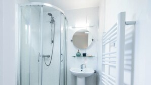 Uma casa de banho moderna com chuveiro em cabine de vidro, lavatório pedestal e porta-toalhas.