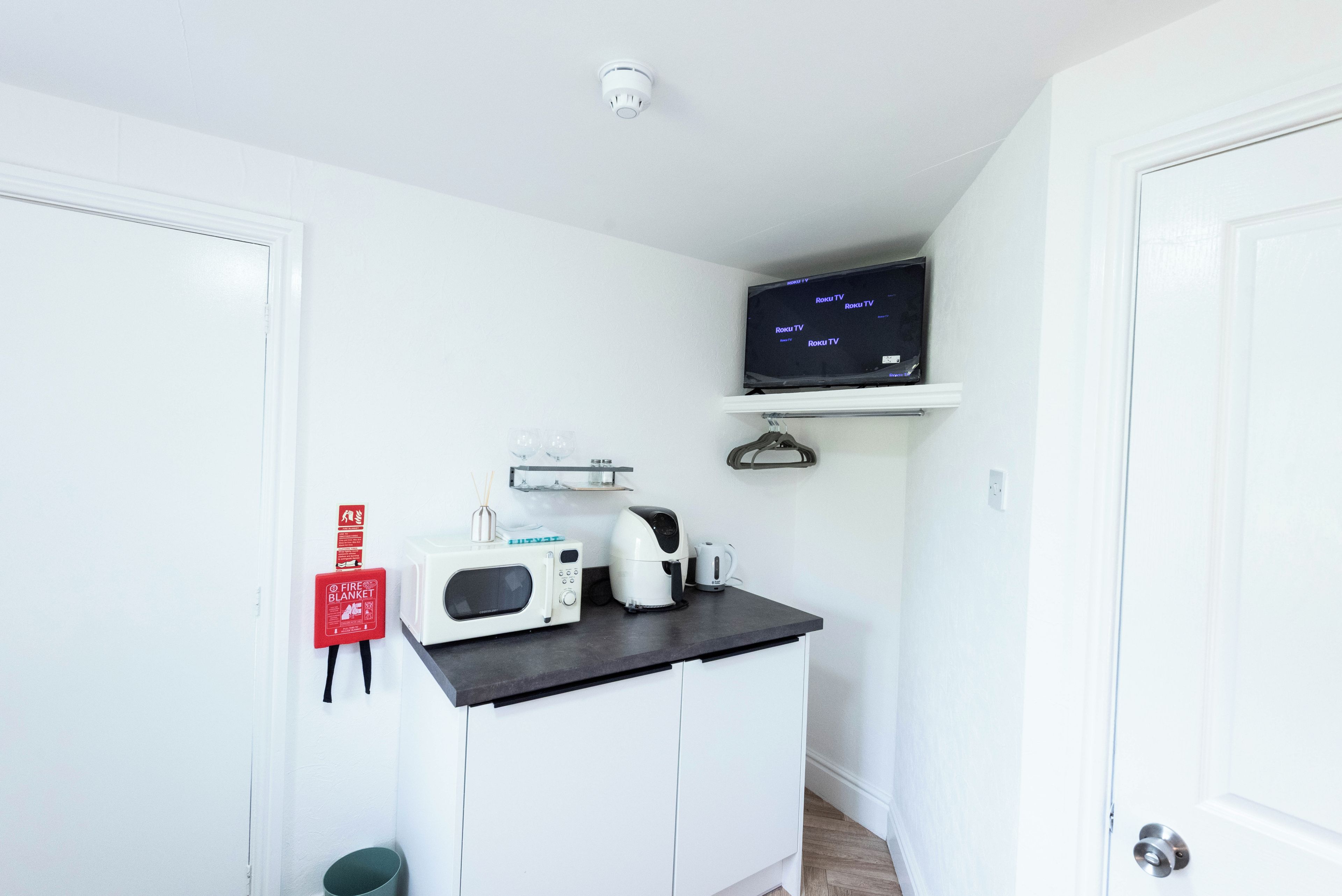 A compact kitchenette with a microwave, kettle, and a flat-screen TV mounted on a shelf.