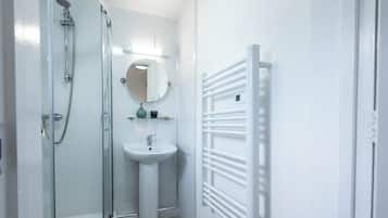 A bathroom with a glass shower enclosure, a pedestal sink, a round mirror, and a white towel rack.