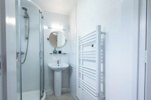 A bathroom with a glass shower enclosure, a pedestal sink, a round mirror, and a white towel rack.